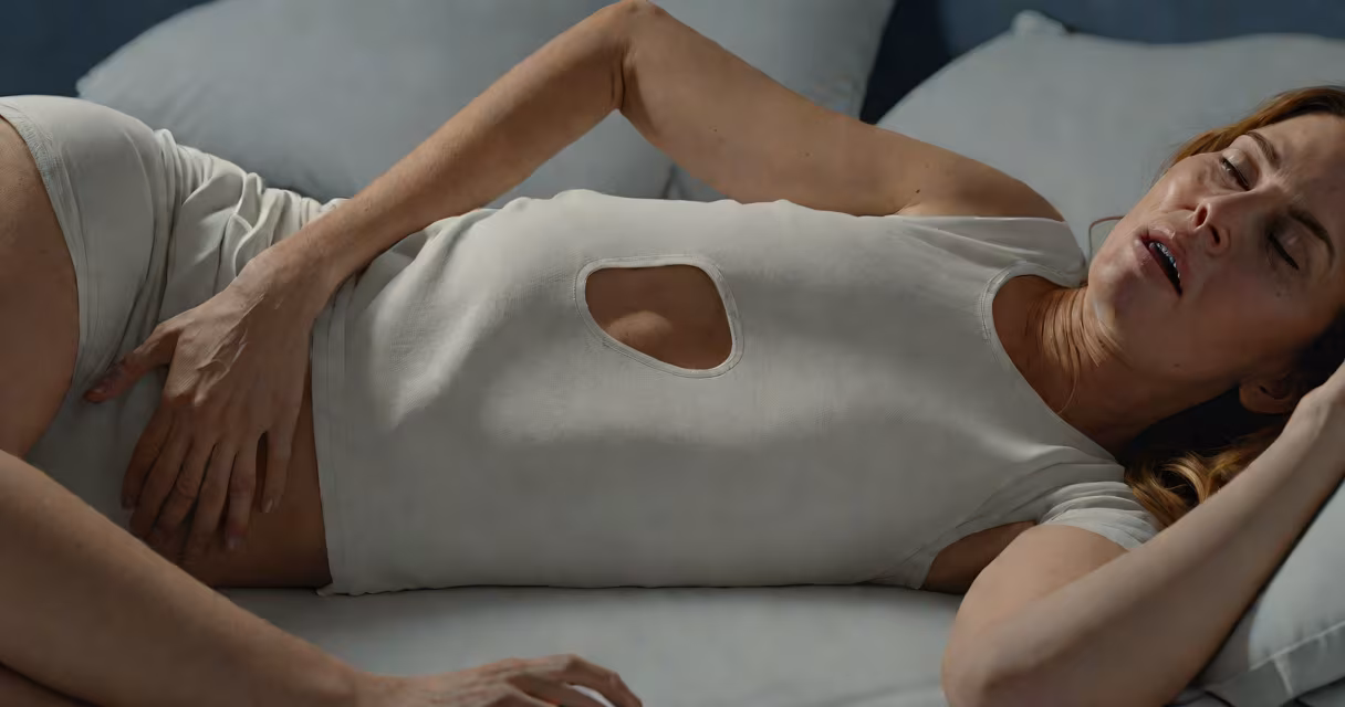 Woman lying on bed clutching abdomen, expression of discomfort, soft lighting