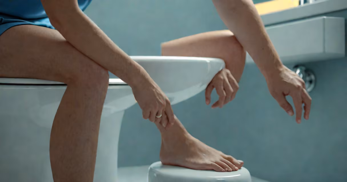 Close-up of a person holding a bathroom sink with a toilet nearby, showing signs of digestive discomfort